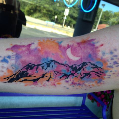 Watercolor style mountain tattoo inside a triangle and